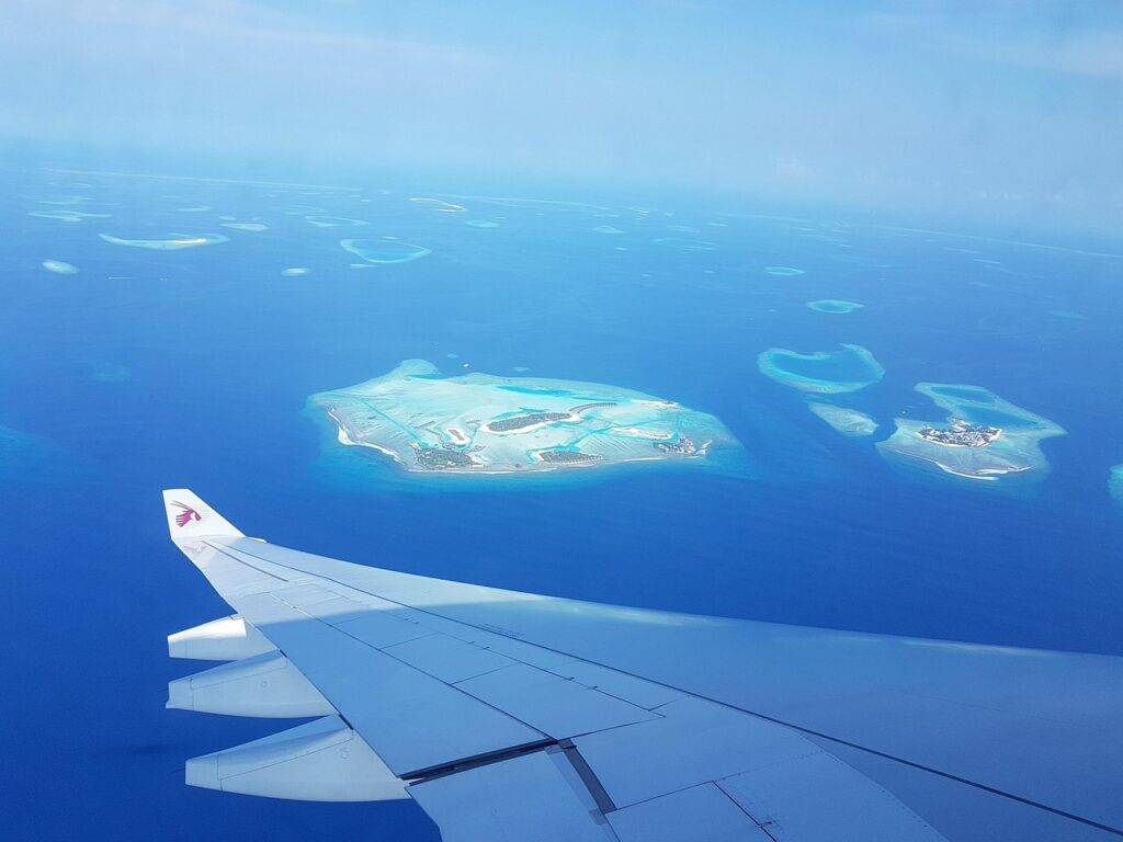 Vista aérea de un grupo de islas rodeadas de aguas turquesas, con un ala de avión en primer plano. La imagen evoca una sensación de tranquilidad y belleza natural.