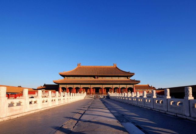 Puente que conduce a un edificio tradicional chino, bajo un cielo azul despejado. La estructura presenta un diseño arquitectónico característico y está rodeada de elementos de piedra.