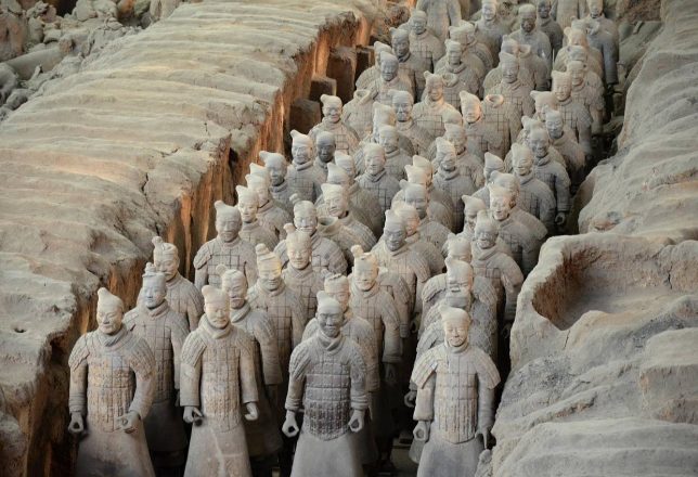 Ejército de terracota en una fosa, mostrando numerosas estatuas de guerreros en formación. Las figuras están esculpidas con detalles y vestimentas de la antigua China.